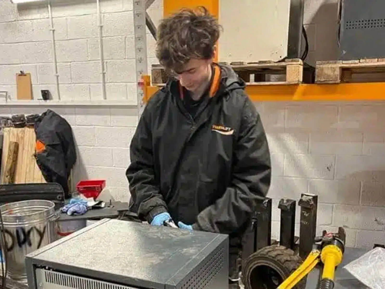 A technician in a black jacket working on computer hardware in a workshop.