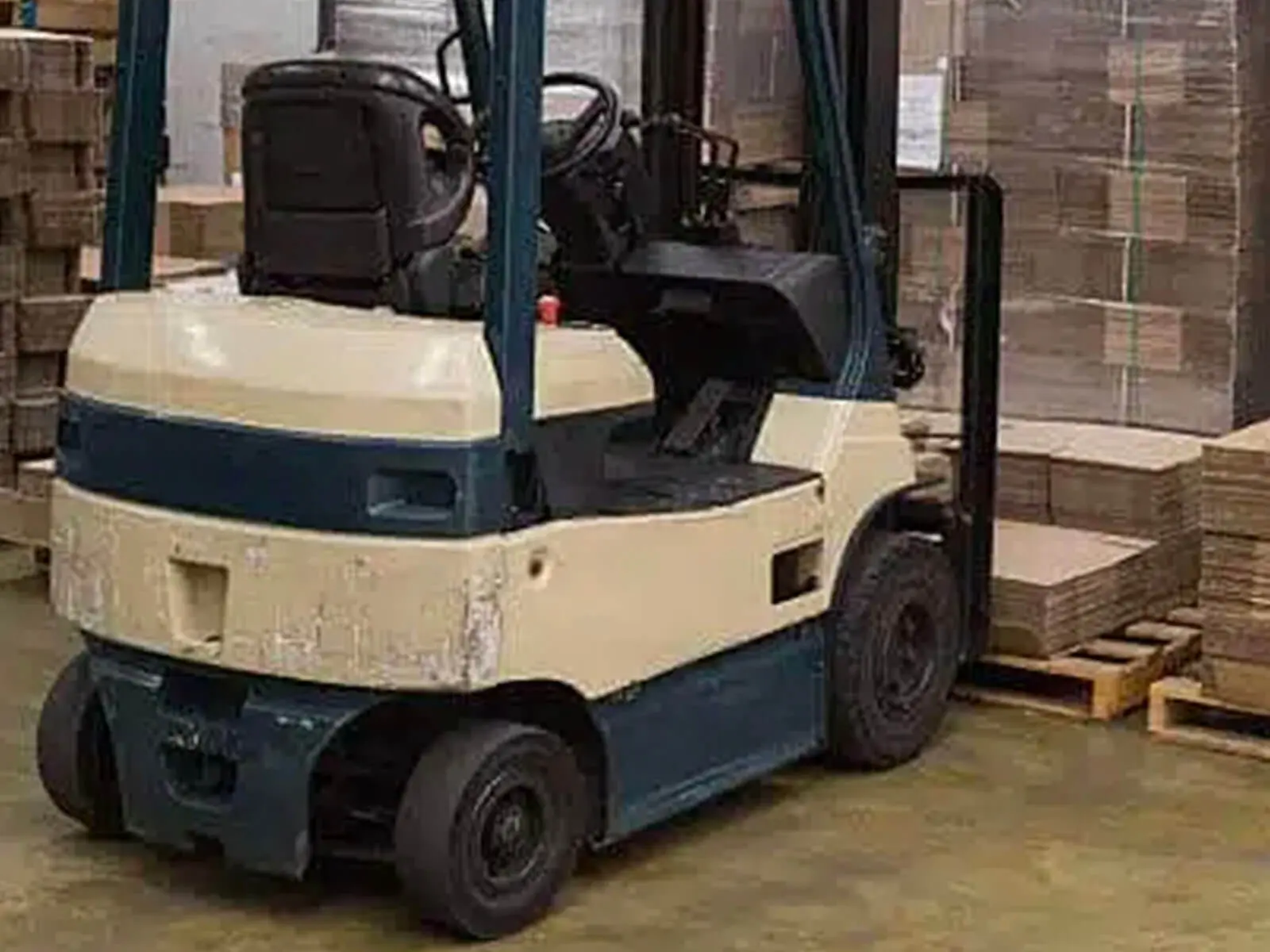 A forklift parked in a warehouse with stacks of cardboard boxes in the background