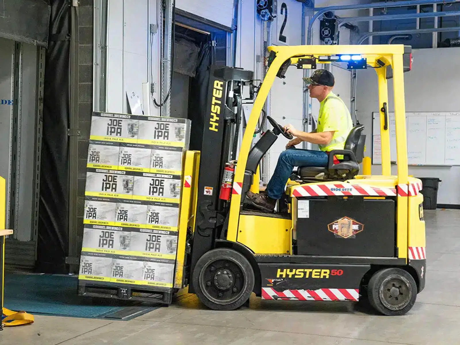 A forklift operated by a worker transports boxes in a warehouse setting.