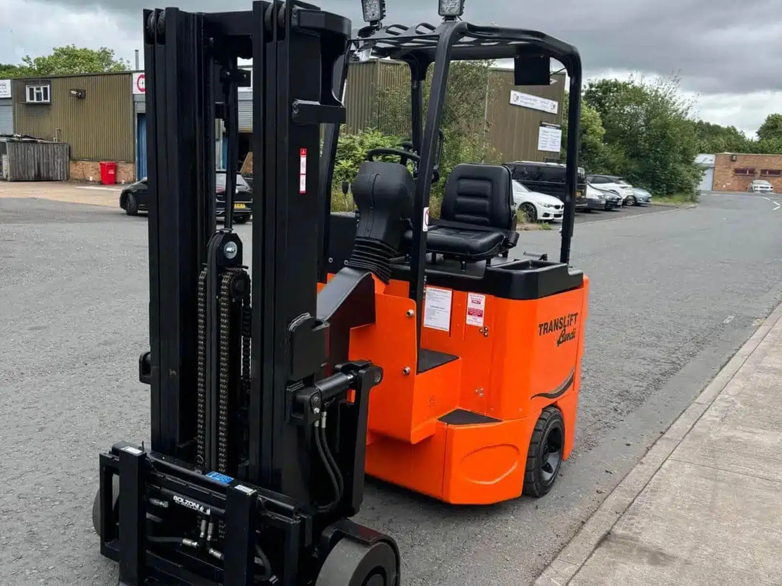 An orange electric forklift truck parked on a street outside a warehouse.