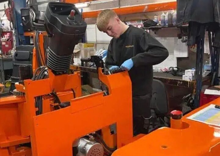 A technician in a workshop inspecting and repairing a piece of industrial machinery, with a focus on the mechanical components.