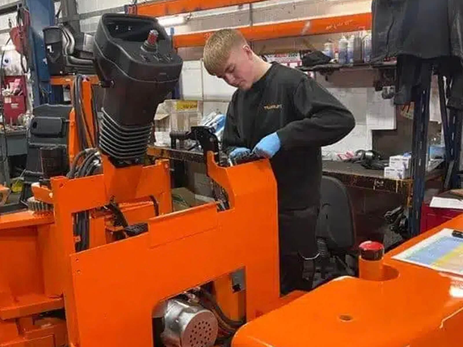 A technician in a workshop inspecting and repairing a piece of industrial machinery, with a focus on the mechanical components.