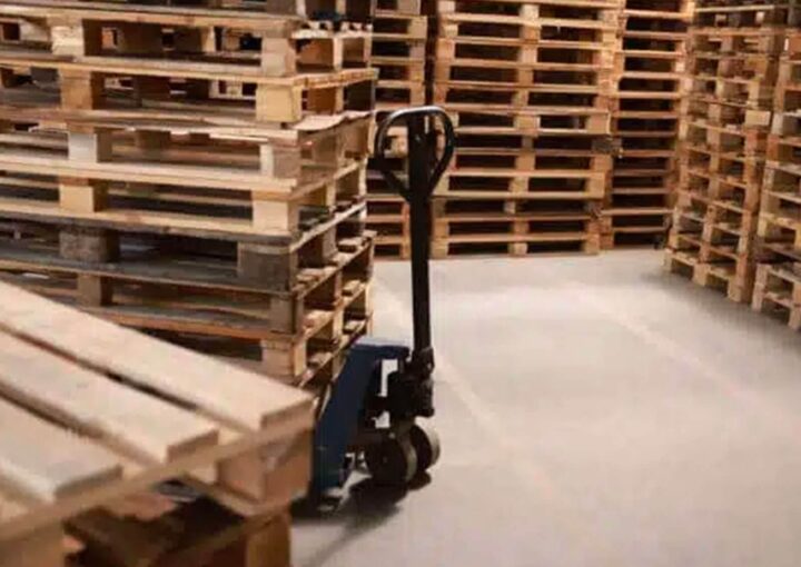 A storage area filled with wooden pallets and a hand pallet truck ready for use.