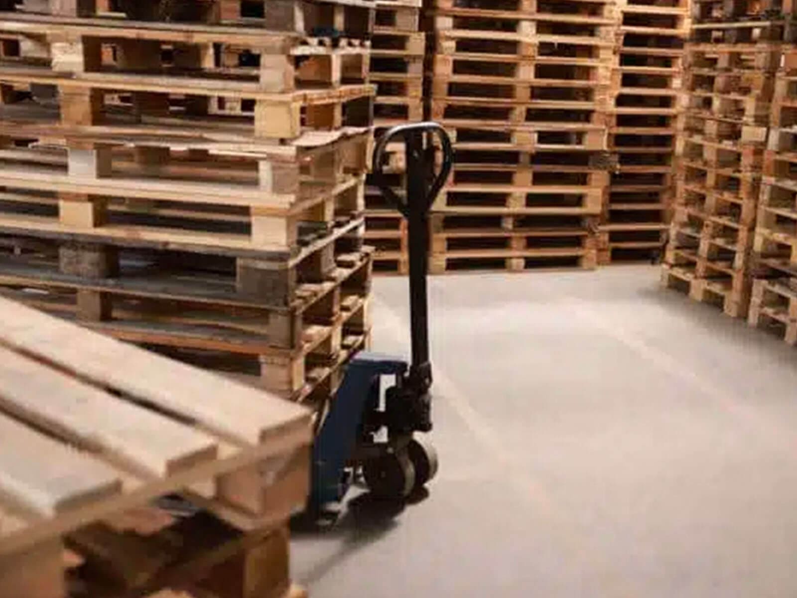 A storage area filled with wooden pallets and a hand pallet truck ready for use.