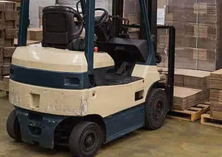A forklift parked in a warehouse with stacks of cardboard boxes in the background