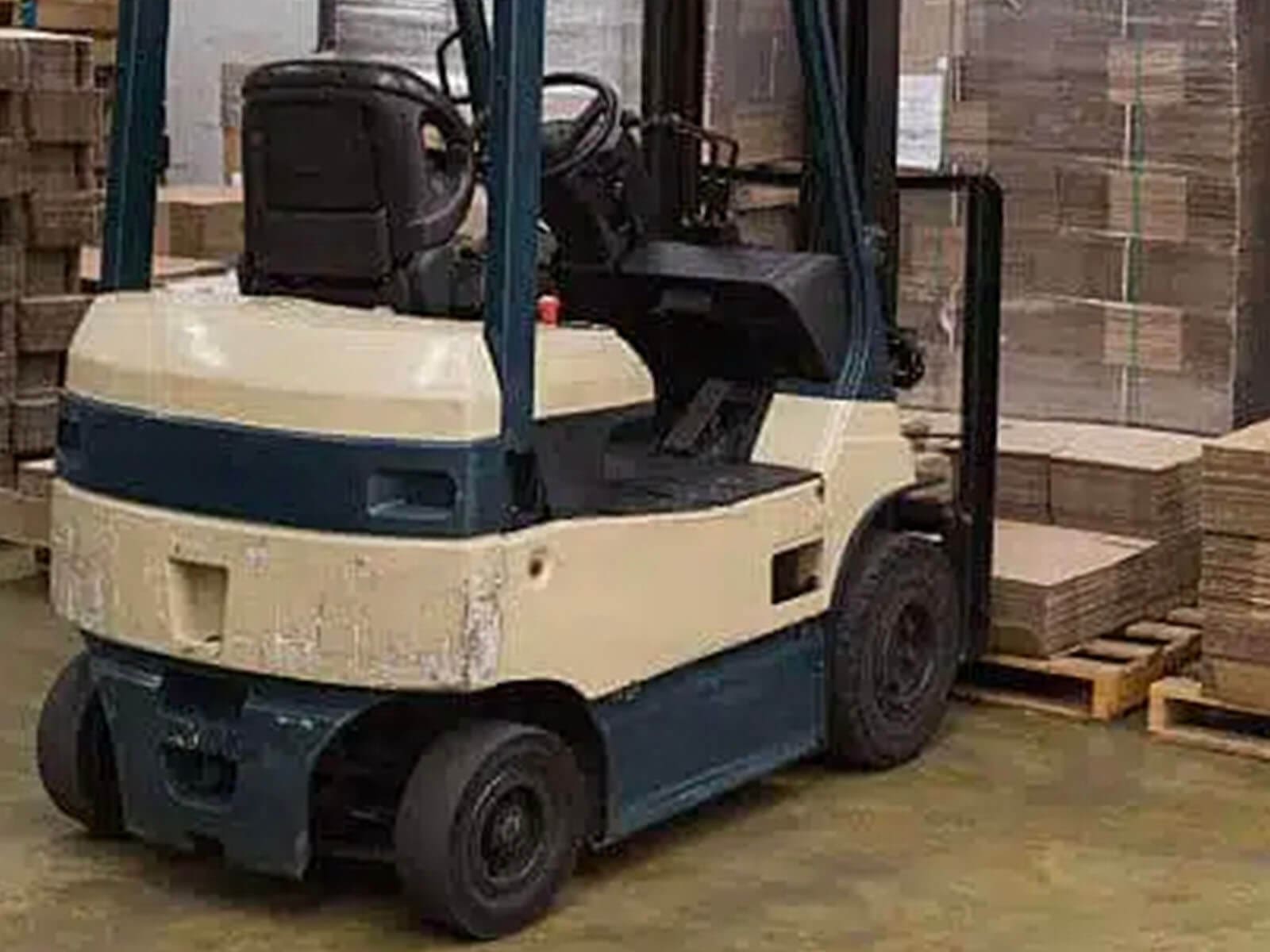 A forklift parked in a warehouse with stacks of cardboard boxes in the background