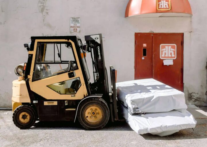 A forklift positioned next to a warehouse door, carrying wrapped materials.