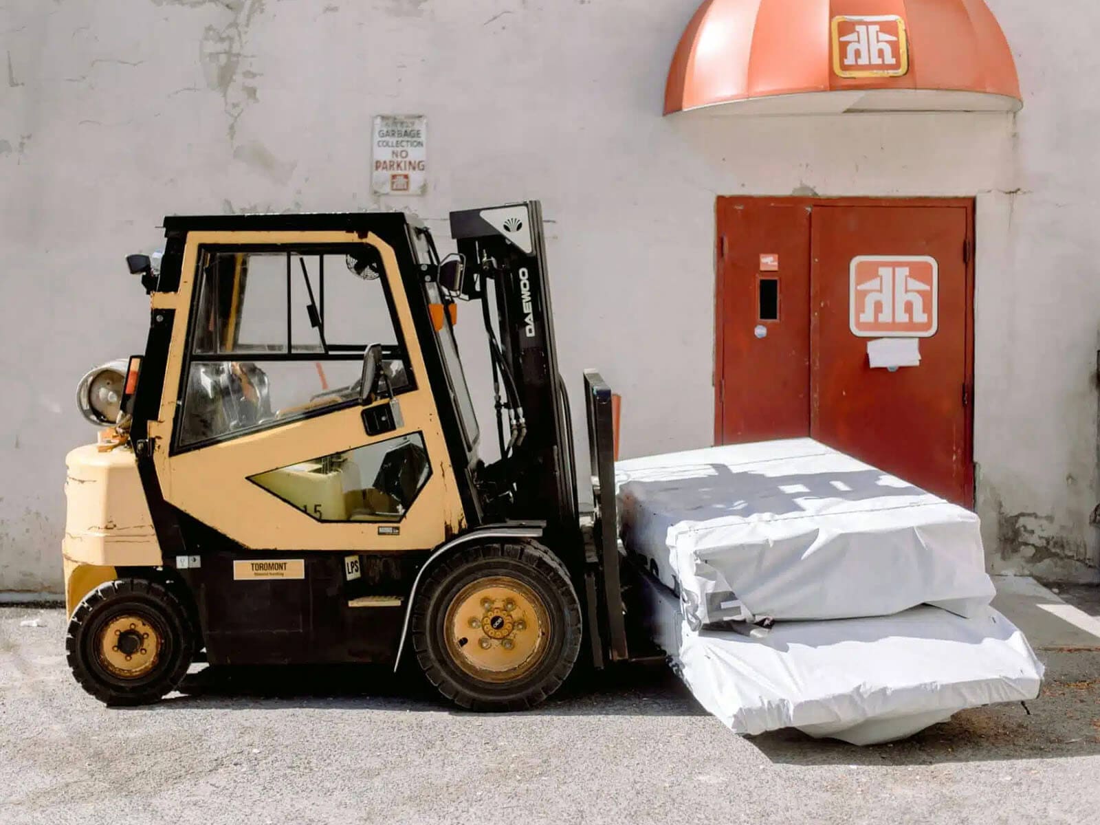 A forklift positioned next to a warehouse door, carrying wrapped materials.
