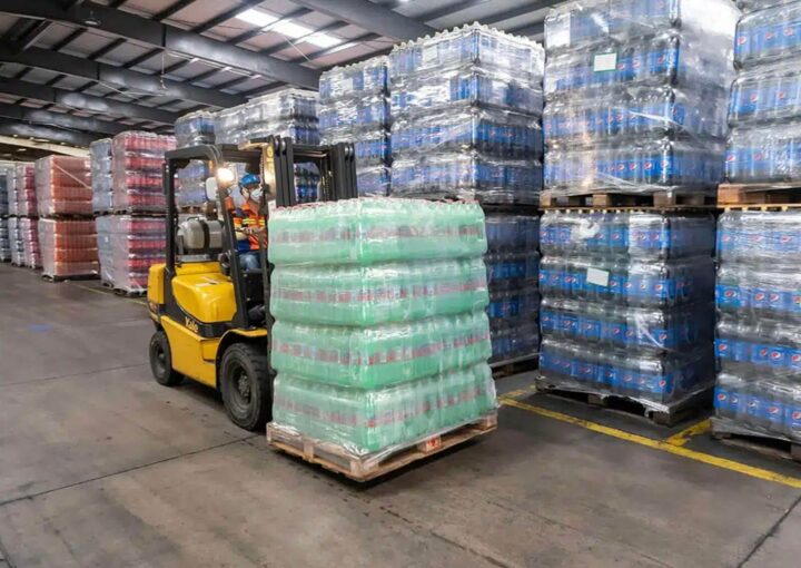 A forklift moving a pallet of goods in a warehouse filled with stacked pallets of various products.