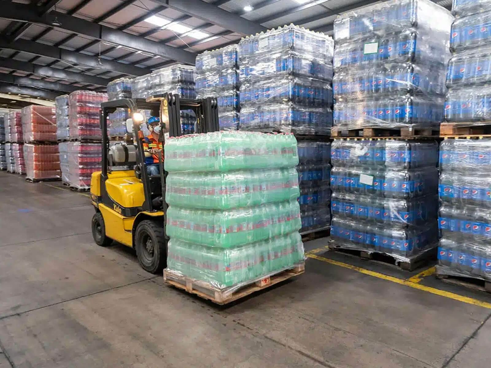 A forklift moving a pallet of goods in a warehouse filled with stacked pallets of various products.