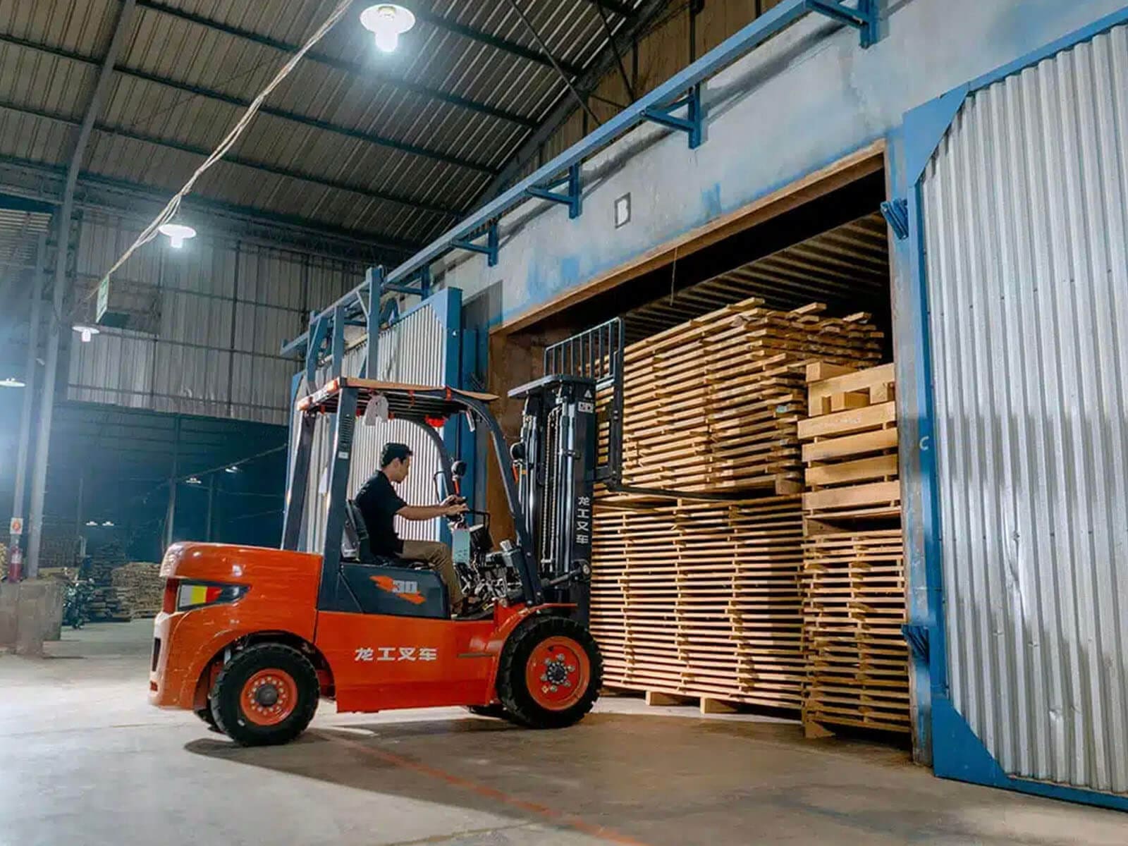 A forklift operator loads stacked wooden pallets inside a warehouse.