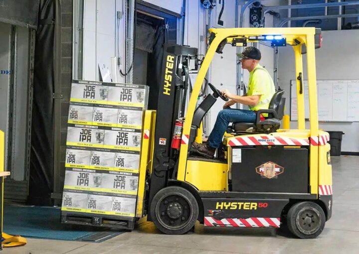 A forklift operated by a worker transports boxes in a warehouse setting.
