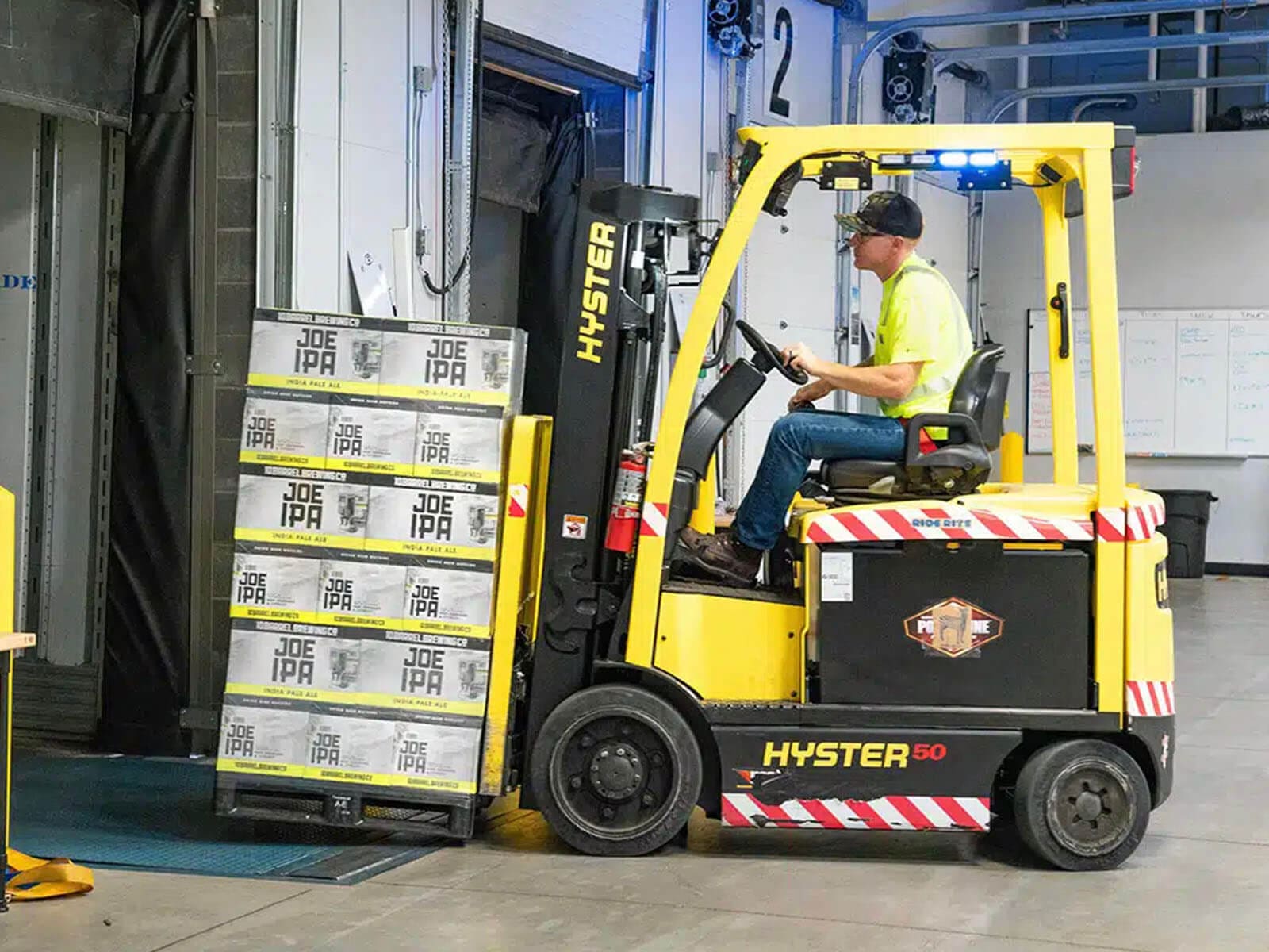 A forklift operated by a worker transports boxes in a warehouse setting.