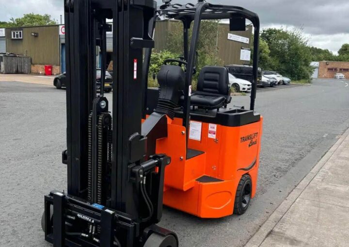 An orange electric forklift truck parked on a street outside a warehouse.