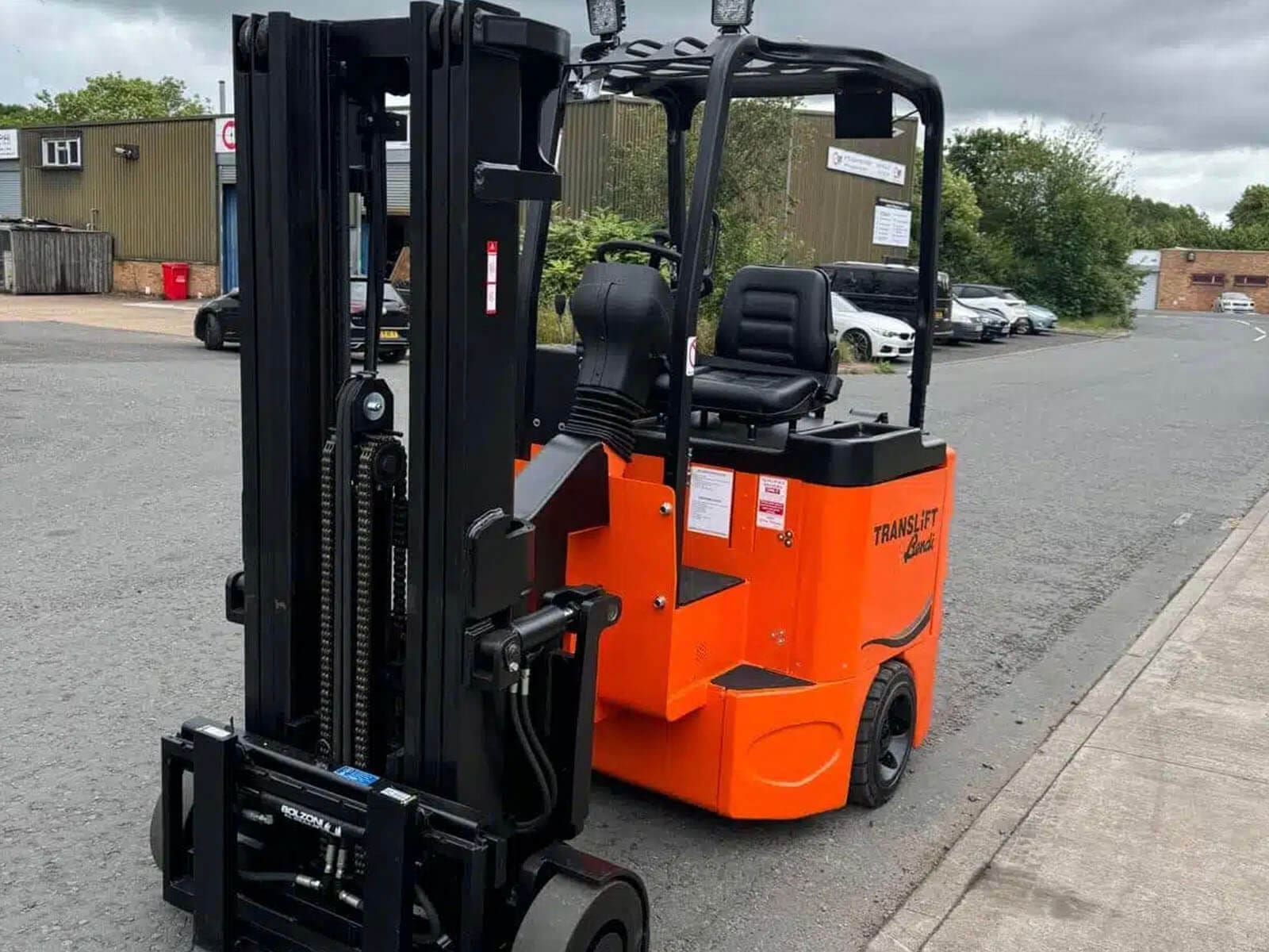 An orange electric forklift truck parked on a street outside a warehouse.